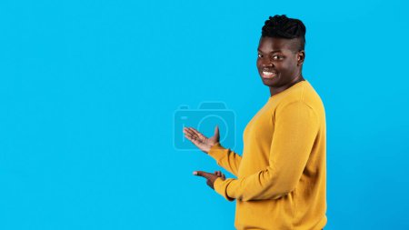 Téléchargez les photos : Handsome Young Black Man Pointing At Copy Space With Two Hands, Happy African American Male Demonstrating Free Place For Design Or Advertisement While Standing Isolated Over Blue Background, Panorama - en image libre de droit