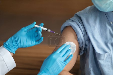 Photo for Unrecognizable Nurse Holding Syringe, Making Vaccine Shot To Shoulder Of Male Patient, Young Man In Medical Mask Getting Vaccinated Against Covid-19 In Clinic, Cropped Image, Closeup - Royalty Free Image