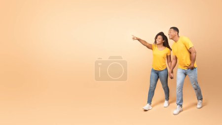 Photo for Happy african american couple walking and holding hands, woman pointing finger to free space, yellow background, panorama. Great ad and offer, romance, love and relationship - Royalty Free Image