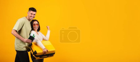 Photo for Cheerful millennial middle eastern lady in glasses with suitcase make victory, male with passports, tickets enjoy travel isolated on orange background, panorama. Sign of success, trip on vacation - Royalty Free Image