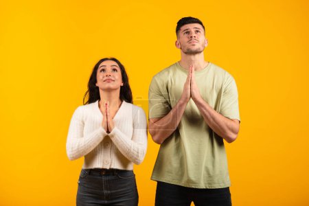 Photo for Serious concentrated millennial arab husband and wife folded hands in supplication, make wish, pray, isolated on orange background, studio. Faith, gratitude, dream, success and victory, ad and offer - Royalty Free Image