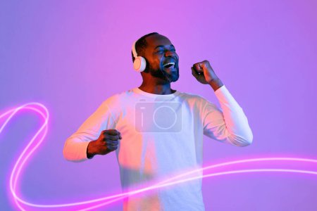 Téléchargez les photos : Joyful happy handsome middle aged bearded african american guy in casual using brand new wireless headphones, listening to music with closed eyes, enjoying sound, neon light background, collage - en image libre de droit