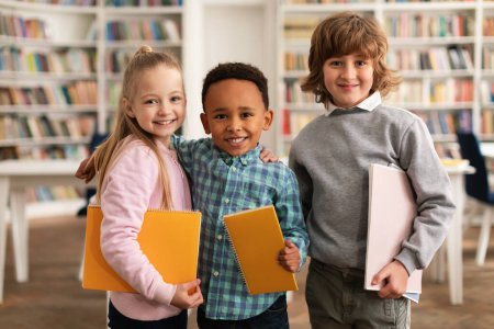 Téléchargez les photos : Ready for school. Portrait of diverse kids posing with notebooks, looking and smiling at camera, standing in modern classroom in school, free space - en image libre de droit