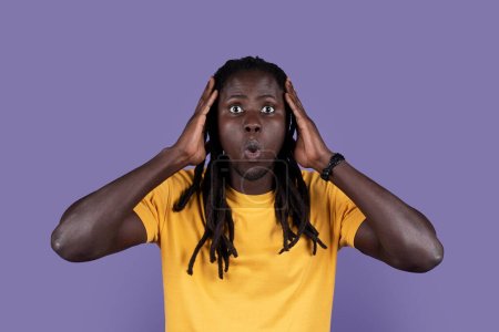 Téléchargez les photos : Shocked attractive long-haired african american millennial man with open mouth touching head, checking something astonishing on purple studio background, closeup portrait. Human emotions concept - en image libre de droit