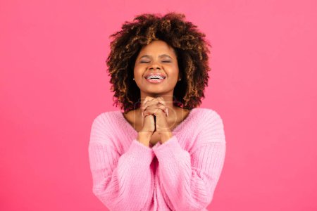 Téléchargez les photos : Happy millennial african american curly lady student in casual with closed eyes crossed arms, made wish isolated on pink background, studio. Prayer gesture, hope for success, desire and lifestyle - en image libre de droit