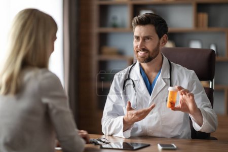 Téléchargez les photos : Smiling Doctor Man Demonstrating Prescribing Medications To Female Patient After Check Up In Clinic, Friendly Male Therapist Holding Bottle With Pills Or Vitamins And Showing It To Young Woman - en image libre de droit