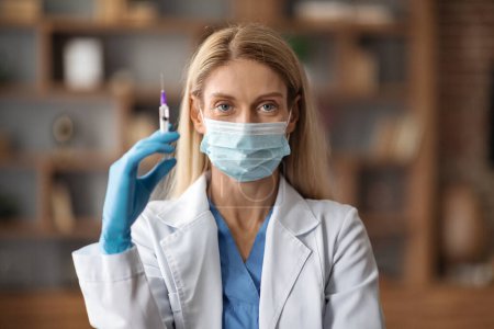 Foto de Immunization Concept. Doctor Lady In Medical Mask Holding Syringe With Vaccine Dose, Physician Woman Wearing Blue Gloves And White Coat Ready To Make Injection Shot, Closeup Portrait - Imagen libre de derechos