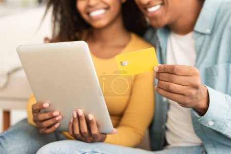 Photo for Happy millennial african american female and guy hugging, using credit card and tablet, ordering purchases in home interior. Financial banking, cashback, shopaholics enjoy sale and online shopping - Royalty Free Image