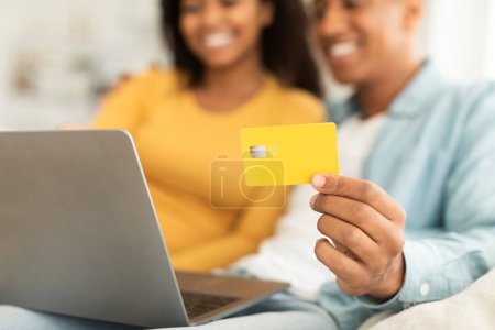 Photo for Glad young african american couple use credit card and laptop, check bank financial account in room interior, cropped, close up. Online shopping, advice sale for shopaholics, ad and offer at home - Royalty Free Image