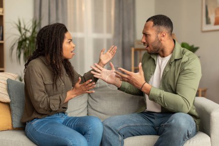 Photo for Emotional african american lovers having quarrel, sitting on sofa in front of each other, yelling and gesturing, experiencing difficulties in marriage - Royalty Free Image