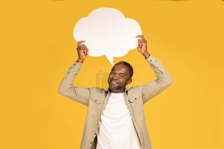 Téléchargez les photos : Cheerful middle aged african american male in casual hold abstract bubble, cloud with empty space for dreams and text, isolated on yellow background, studio. Recommendation, advice, ad and offer - en image libre de droit