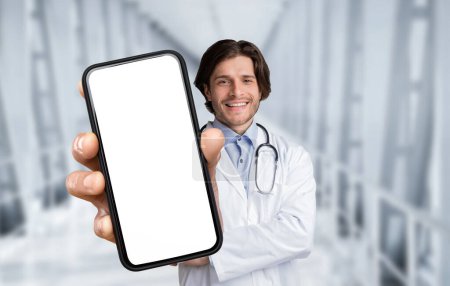 Photo for Handsome Male Doctor In Uniform Holding Big Blank Smartphone In Hand While Posing In Hospital Hall, Smiling Physician Man Recommending Medical App Or Advertising Health Insurance, Collage, Mockup - Royalty Free Image