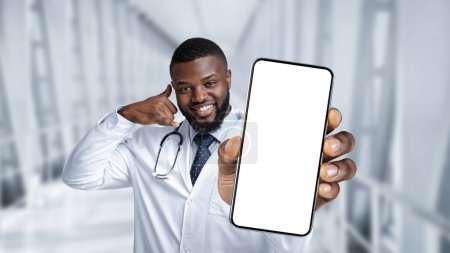 Téléchargez les photos : Online Medical Support. Black Doctor Holding Blank Smartphone And Showing Call Me Gesture While Standing In Clinic Hall, Smiling Male Physician Advertising Modern App Or Website, Collage, Mockup - en image libre de droit