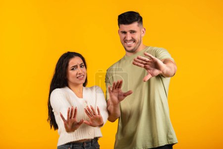 Foto de Displeased sad millennial arabic husband and wife make stop gesture with hands, push back camera, isolated on orange background, studio. Disgust, sign of personal space, say no and negative emotion - Imagen libre de derechos