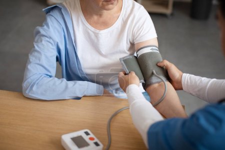 Photo for Doctor measures blood pressure with tonometer of senior european female patient in clinic office interior, cropped. Health care, treatment of high pressure, visit to therapist and medical examination - Royalty Free Image