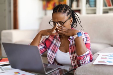 Foto de Overworked exhausted young black woman freelancer sitting on floor in front of laptop, rubbing her face, removing eyeglasses, feeling tired, home interior, copy space. Burnout in millennials concept - Imagen libre de derechos