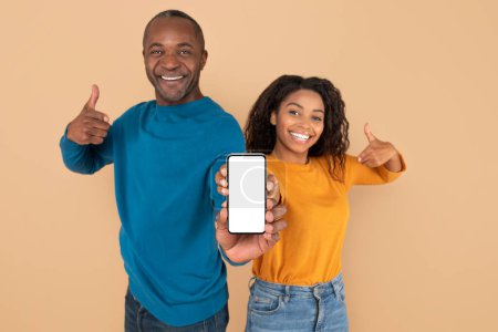 Téléchargez les photos : Use this new cool app. Excited black couple pointing at smartphone with blank screen, recommending application, advertising your website, mockup for design - en image libre de droit