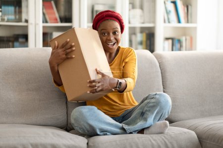 Téléchargez les photos : Overjoyed emotional young black woman customer receive good parcel cardboard box at home satisfied with great purchase, happy lady consumer hugging package postal shipping delivery, copy space - en image libre de droit