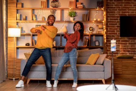 Photo for African american couple recording video content, dancing on smartphone camera at home. Positive black boyfriend and girlfriend filming for social media, using mobile device. Vlogging concept - Royalty Free Image