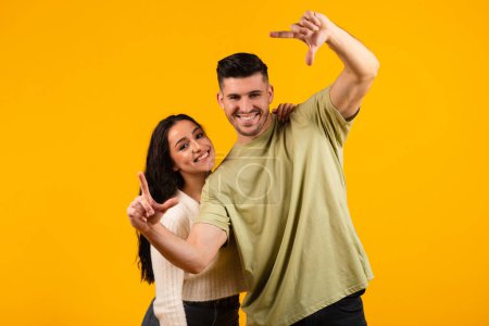 Foto de Happy millennial arabic husband and wife make hands lens, look through foreshortening isolated on orange background, studio. Family relationships, filming with objective for idea, dream, ad and offer - Imagen libre de derechos