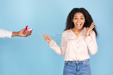 Photo for Marriage proposal, engagement, surprise concept. Black man giving ring in box to shocked lady with open mouth, blue background, studio shot, copy space - Royalty Free Image