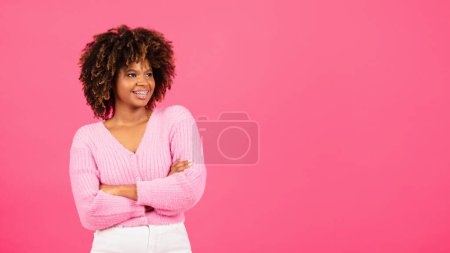 Téléchargez les photos : Happy millennial african american curly lady in casual with crossed arms looking at empty space isolated on pink background, studio. Good advertisement and offer, fashion blog and beauty, lifestyle - en image libre de droit
