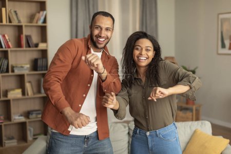 Photo for Joyful african american spouses having fun and dancing together, celebrating move or anniversary in living room interior. Couple enjoying free time at home - Royalty Free Image