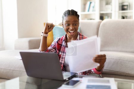 Photo for Emotional cheerful young african american lady in casual entrepreneur working from home, sitting on floor by couch, using laptop, looking at papers correspondence, gesturing, business income, profit - Royalty Free Image