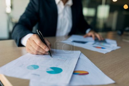 Photo for Male business analyst writing on papers, checking data, charts and graphs, sitting at desk in office, closeup, cropped. Man monitoring company growth, profit and analyzing - Royalty Free Image