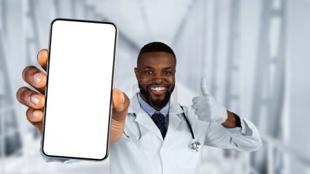 Téléchargez les photos : Smiling Black Doctor Man Showing Blank Smartphone At Camera And Gesturing Thumb Up While Standing Over Clinic Hall Background, African American Male Therapist Recommending New App, Collage, Mockup - en image libre de droit