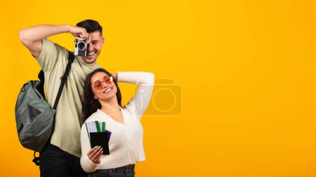 Téléchargez les photos : Satisfied millennial arab woman in glasses with passports and tickets and guy traveler with backpack and camera enjoy journey isolated on orange background, studio, panorama. Travel on vacation, trip - en image libre de droit