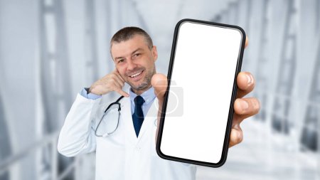 Téléchargez les photos : Smiling middle aged male doctor showing blank smartphone and making call me gesture, friendly therapist man in uniform holding phone with white screen while standing in hospital hall, collage, mockup - en image libre de droit
