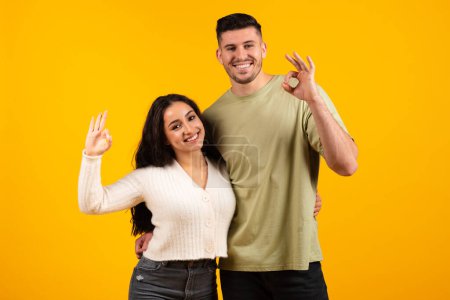 Téléchargez les photos : Smiling millennial arabic female and male making ok sign with hands, recommend and advice for family, isolated on orange background, studio, copy space. Love and romance, great sale, ad and offer - en image libre de droit