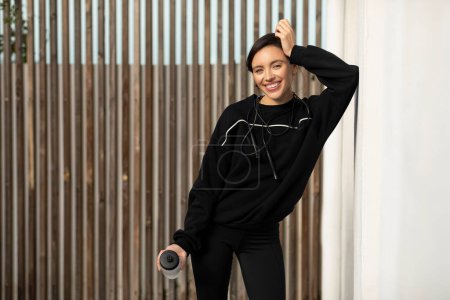 Téléchargez les photos : Smiling muscular slim young european lady athlete in black sportswear with water bottle and skipping rope, enjoy weight loss, fitness in city, outside. Break, health care, muscle training and sport - en image libre de droit