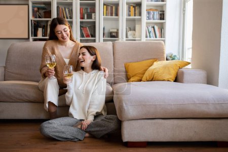 Téléchargez les photos : Glad laughing european millennial girlfriends cheers glasses of wine, enjoy rest, relax and free time together, celebrate holiday in comfort living room interior. Event, toast, date and party at home - en image libre de droit