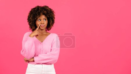 Foto de Pensive millennial african american curly woman in casual looking at empty space, thinking isolated on pink background, studio. Idea creating, brainstorm, ad and offer, fashion blog and lifestyle - Imagen libre de derechos