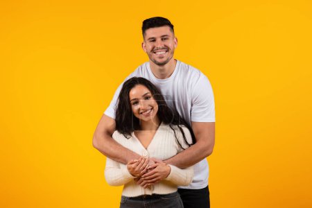 Téléchargez les photos : Happy family relationships. Cheerful young arab guy hugging female, enjoy tender moment, have fun, look at camera isolated on yellow background, studio. Love couple, lifestyle, date, ad and offer - en image libre de droit