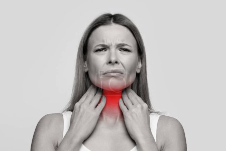 Foto de Unhappy middle aged woman suffering from pain in throat, touching inflamed zone on her neck, empty space, studio background, black and white photo. Cold, flu, pharyngitis, allergy concept - Imagen libre de derechos