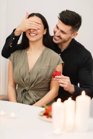 Photo for Valentine gift concept. Attractive cheerful brunette guy surprising beautiful girlfriend with present, man cover woman eyes with palm, holding red gift box and smiling, vertical shot - Royalty Free Image