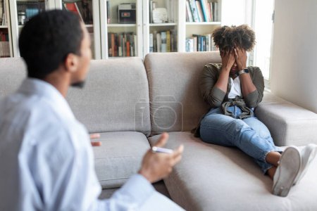 Foto de Millennial black man in formal outwear psychologist have conversation with frustrated unhappy crying young african american woman, therapist talking to upset patient, taking notes, copy space - Imagen libre de derechos