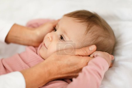 Foto de Mother and kid concept. Loving mom cuddling with her beautiful little baby girl at home, lying on bed, closeup. Woman touching cheeks of her pretty kid - Imagen libre de derechos