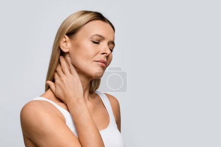Photo for Tired upset attractive middle aged blonde woman massaging her neck with closed eyes over grey studio background, suffering from neck pain, copy space. Mental stress, physical strain, osteoarthriris - Royalty Free Image
