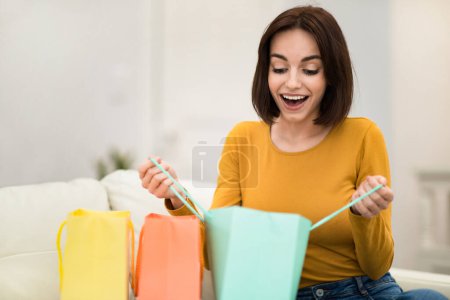 Foto de Overjoyed emotional pretty young woman customer receive good shopping bags at home satisfied with great purchase, happy lady consumer checking colorful paper bags shipping delivery, copy space - Imagen libre de derechos