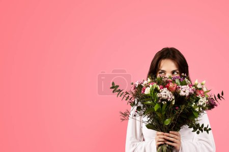 Téléchargez les photos : Cheerful young caucasian woman in casual enjoy aroma of bouquet of flowers, rejoices gift, isolated on pink background, studio. Lifestyle, emotions from celebration of holiday, birthday in spring - en image libre de droit