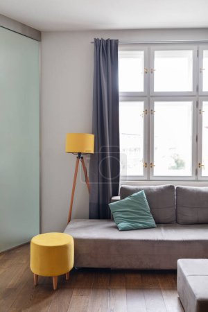 Photo for Stylish Minimalistic Furniture In Modern Living Room Interior, Closeup Shot Of Cozy Room With Big Grey Sofa, Yellow Pouf Chair, Lamp And Panoramic Window, Contemporary Design In Flat - Royalty Free Image