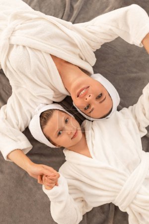 Téléchargez les photos : Young Beautiful Mother And Cute Preteen Daughter Wearing Bathrobes And Towels On Head Lying On Bed, Happy Mom And Female Child Relaxing Together After Bath, Ready For Spa Beauty Treatments, Top View - en image libre de droit