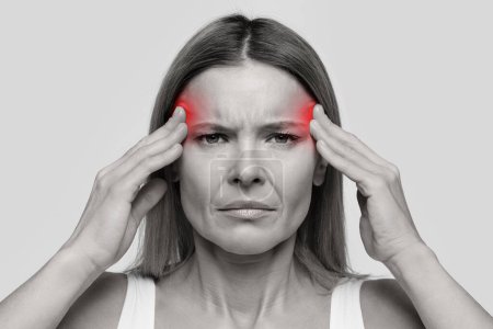 Photo for Unhappy stressed middle aged woman with headache touching inflamed zones her temples, isolated on studio background, emotional black and white closeup photo - Royalty Free Image