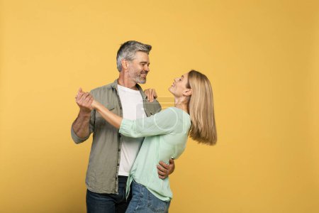 Téléchargez les photos : Loving middle aged spouses dancing and having fun over yellow studio background, free space. Husband and wife having date. Romantic relationship and happy marriage concept - en image libre de droit