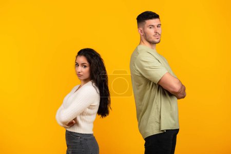 Photo for Sad offended young middle eastern woman ignores boyfriend in casual with crossed arms, think about divorce isolated on yellow background, studio. Relationship problems, quarrel, emotions and breakup - Royalty Free Image