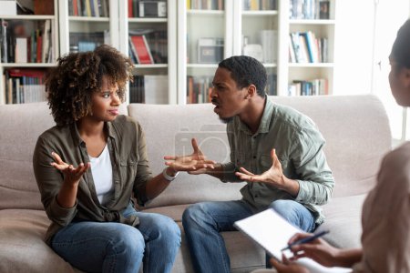 Foto de Hysterical emotional young black man and woman yelling and gesturing, african american spouses fight at family counselor office. Marital crisis, marriage counseling concept - Imagen libre de derechos